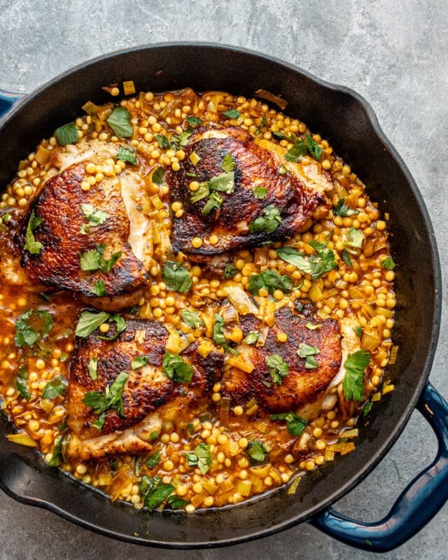 Harissa spiced chicken thighs in a skillet with couscous and a garnish of parsley.