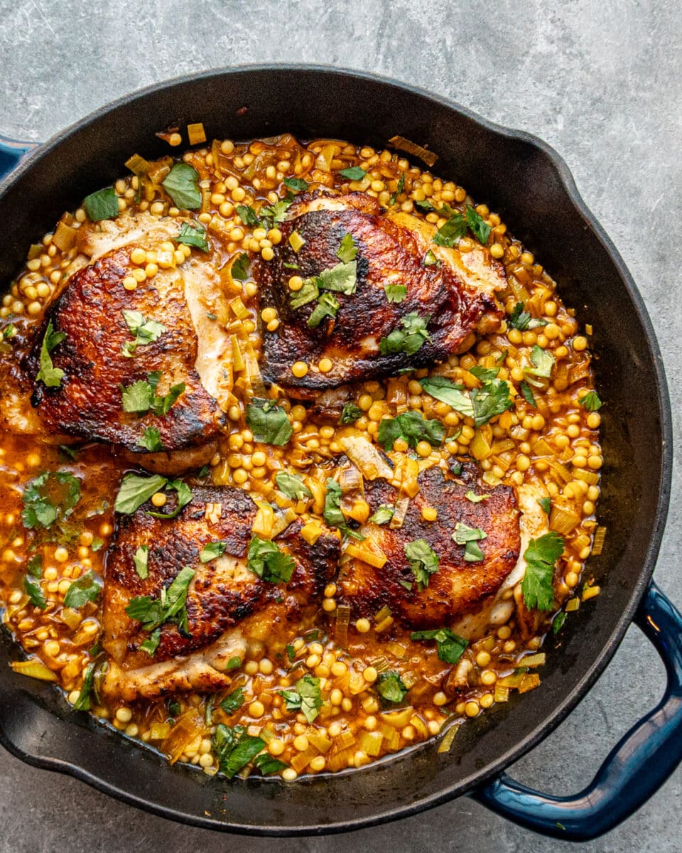 Harissa spiced chicken thighs in a skillet with couscous and a garnish of parsley.