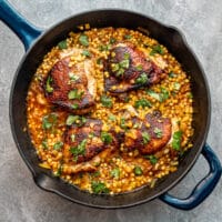 Harissa spiced chicken thighs in a skillet with couscous and a garnish of parsley.