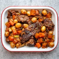 A Yankee pot roast in a tray surrounded by vegetables.