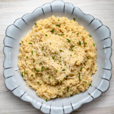 A serving bowl of creamy pastina with Parmesan cheese and chives for garnish.