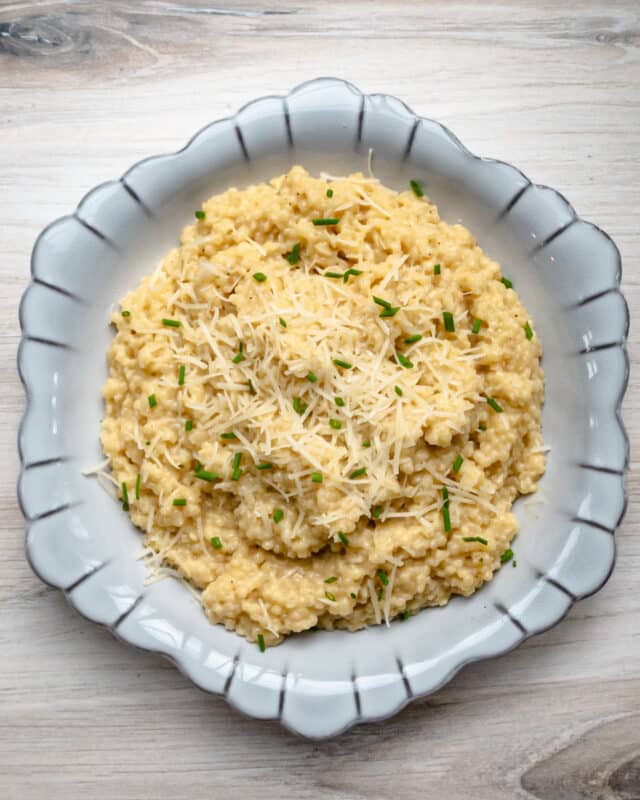 A serving bowl of creamy pastina with Parmesan cheese and chives for garnish.