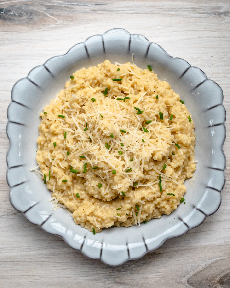 A serving bowl of creamy pastina with Parmesan cheese and chives for garnish.