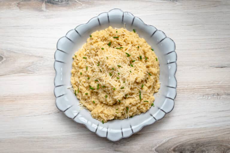 A serving bowl of pastina garnished with extra Parmesan cheese and snipped chives.