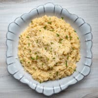 A bowl of pastini, garnished with extra Parmesan cheese and chives.