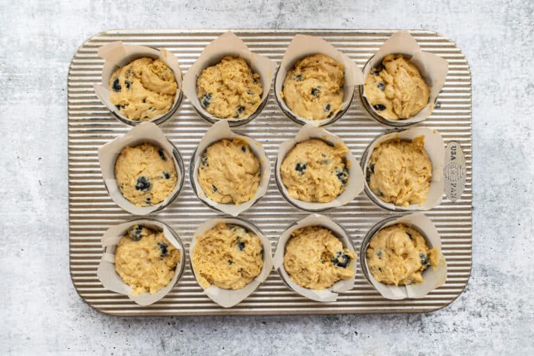 Parchment paper lined muffin cups are filled with the blueberry muffin batter.