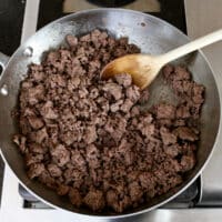 Browning ground beef in a stainless steel pan, with wooden spoon.