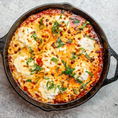 A lazy skillet lasagna with ravioli and sauce, garnished with basil.
