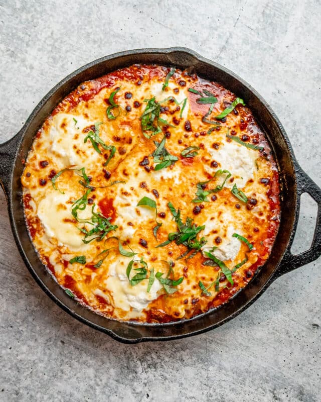 A lazy skillet lasagna with ravioli and sauce, garnished with basil.