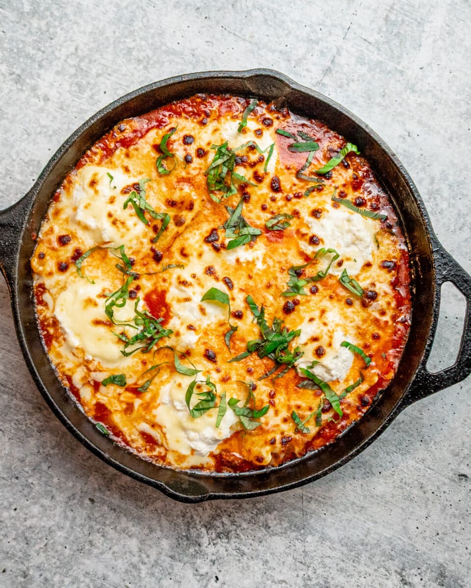 A lazy skillet lasagna with ravioli and sauce, garnished with basil.