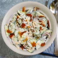 A serving bowl with ranch cucumber salad, with dill and bacon garnish.