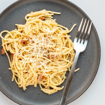 Overhead photo of spaghetti carbonara with fork and parmesan garnish.