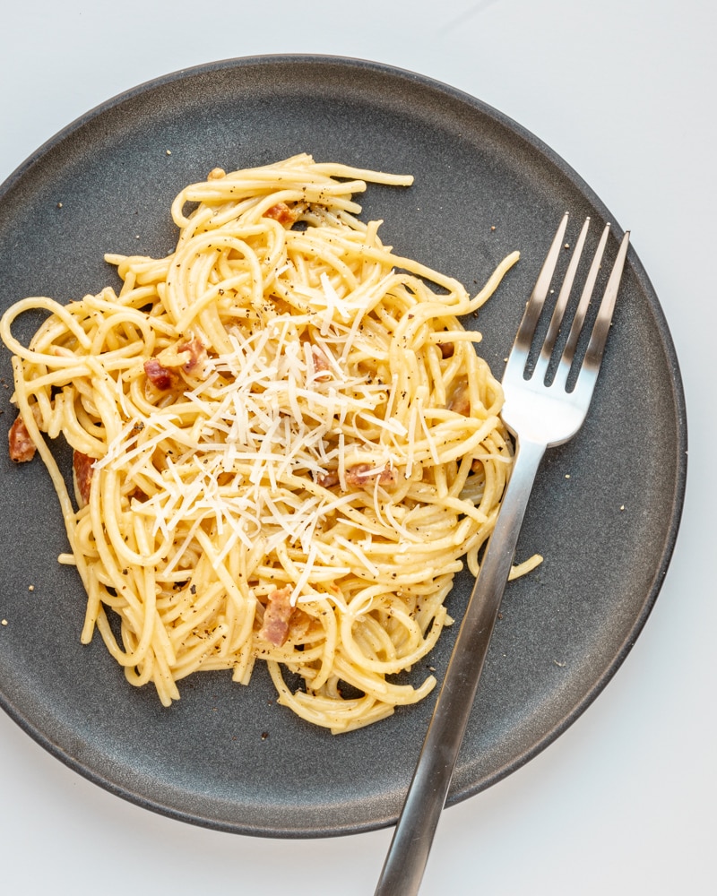 Overhead photo of spaghetti carbonara with fork and parmesan garnish.