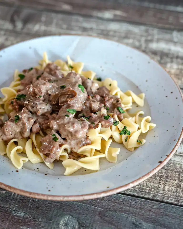 Creamy mushroom sauce over buttered egg noodles, garnished with fresh herbs.