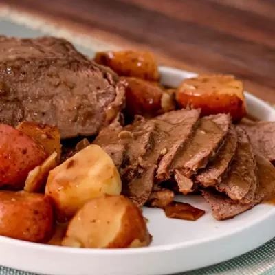 Roast beef with potatoes and carrots on a white plate.