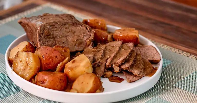 Roast beef with potatoes and carrots on a white plate.