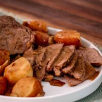 Sliced slow cooker pot roast in a plate with potatoes and gravy.
