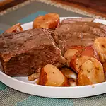 Roast beef with roasted potatoes and sweet potatoes on a white plate.