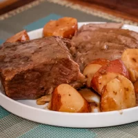 Roast beef with roasted potatoes and sweet potatoes on a white plate.