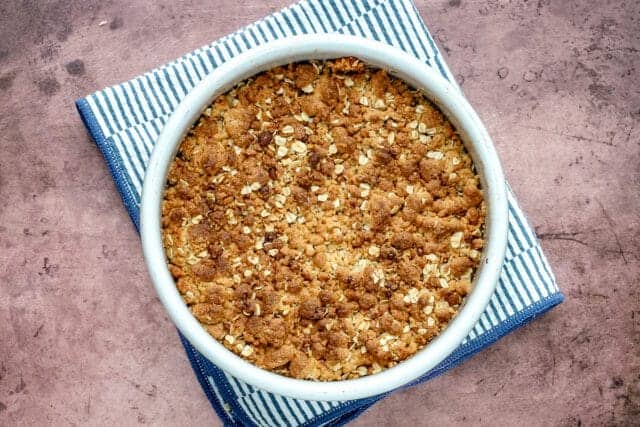 Golden apple crumble topped with chopped nuts on a blue-striped cloth.
