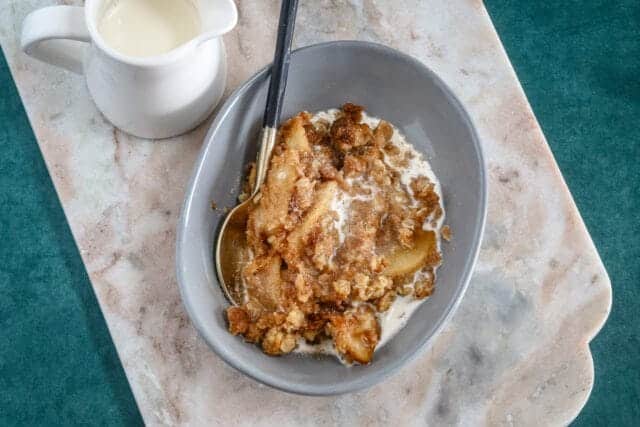A dessert dish with apple crumble and a small pitcher of cream for drizzling.