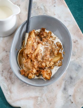 A dessert dish with apple crumble and a small pitcher of cream for drizzling.