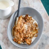 A dessert dish with apple crumble and a small pitcher of cream for drizzling.