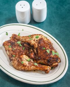 Air fryer chicken legs on a small platter garnished with parsley, with salt and pepper shakers in the background.