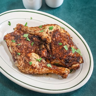 Air fryer chicken legs on a small platter garnished with parsley, with salt and pepper shakers in the background.