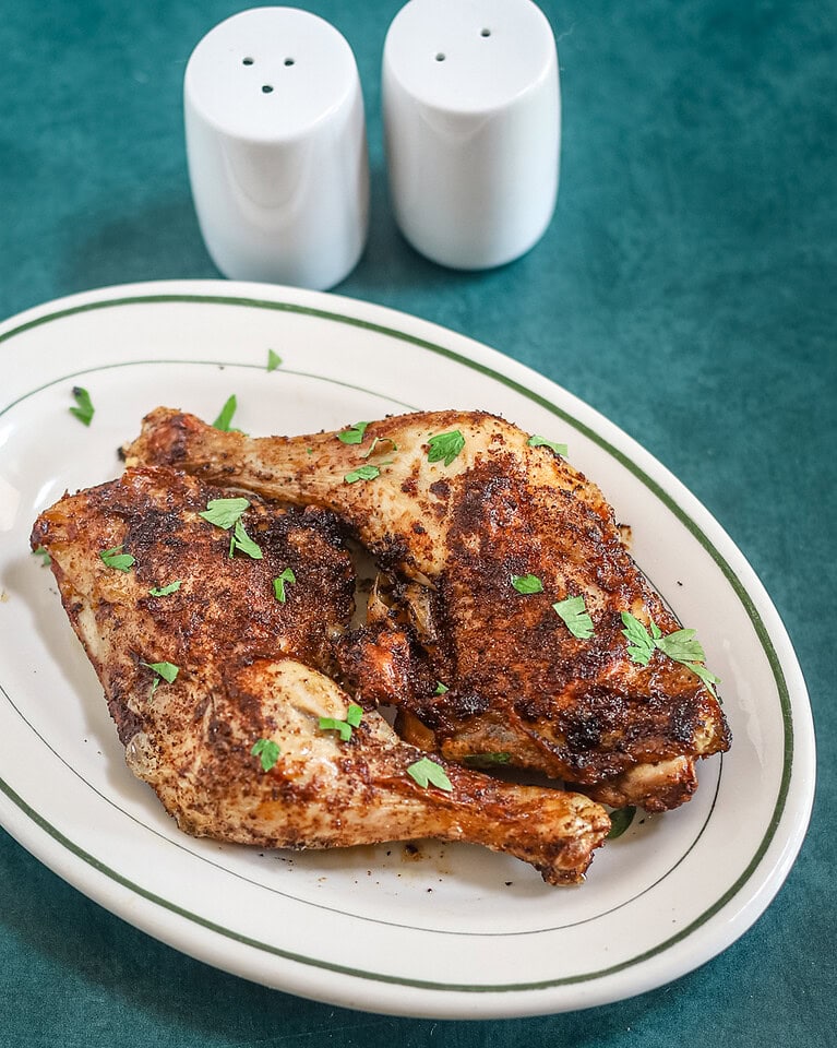Air fryer chicken legs on a small platter garnished with parsley, with salt and pepper shakers in the background.
