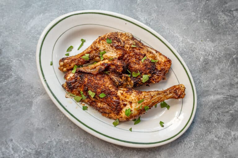 Air fryer chicken legs on a small platter garnished with parsley, with salt and pepper shakers in the background.