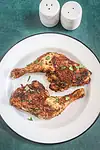 Air fryer chicken legs on a small platter garnished with parsley, with salt and pepper shakers in the background.