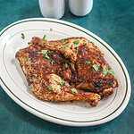 Air fryer chicken legs on a small platter garnished with parsley, with salt and pepper shakers in the background.