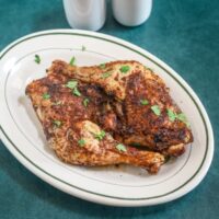 Air fryer chicken legs on a small platter garnished with parsley, with salt and pepper shakers in the background.