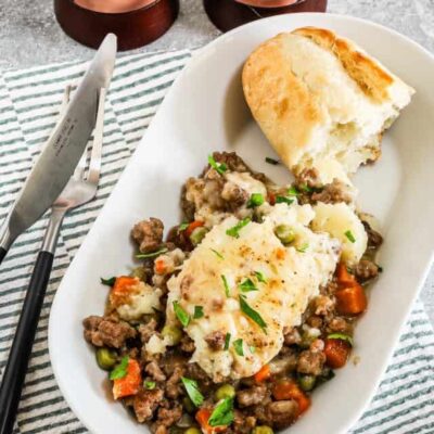 Creamy mashed potatoes with ground beef and vegetables on a white oval plate.