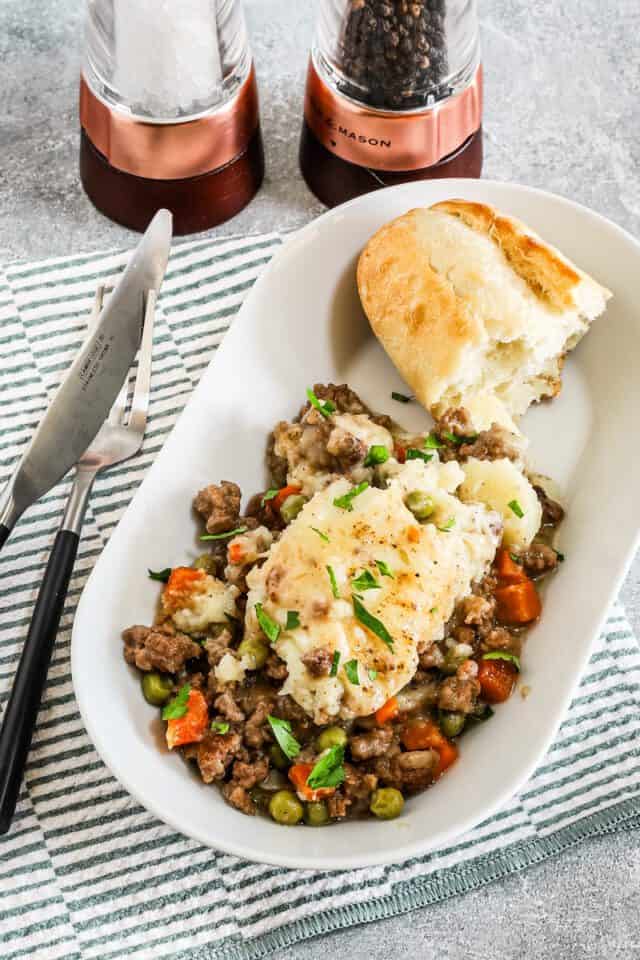Creamy mashed potatoes with ground beef and vegetables on a white oval plate.