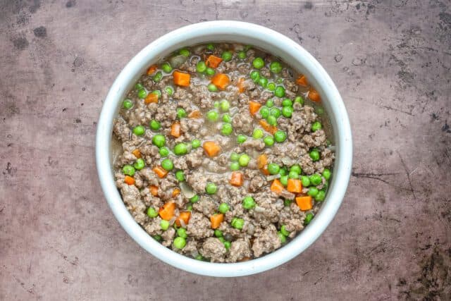 Minced ground beef with green peas and diced carrots in a white bowl.