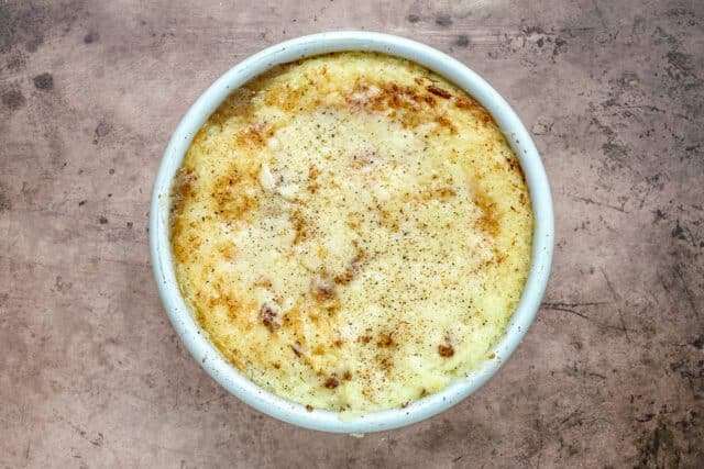 Creamy baked mac and cheese in a white ramekin on a rustic surface.