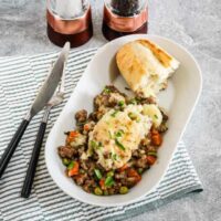 Savory meat pie served with mashed potatoes and vegetables on a white dish.