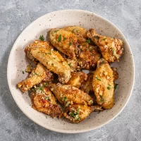 Crispy baked chicken wings garnished with parsley and grated cheese.