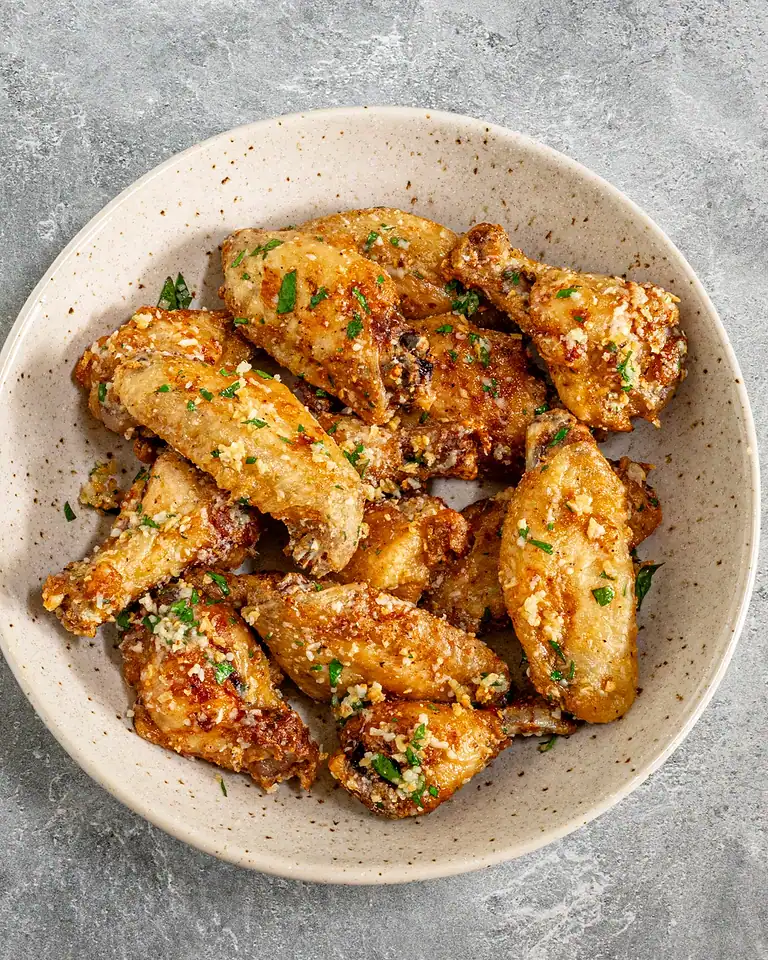 Crispy baked chicken wings garnished with chopped herbs and garlic crumbs.