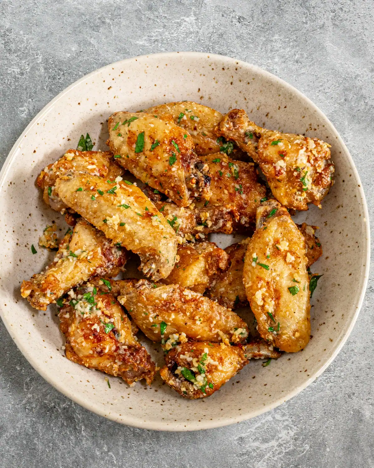 Crispy baked chicken wings garnished with chopped herbs and garlic crumbs.