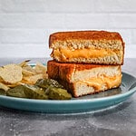 A grilled cheese sandwich from the air fryer, sliced and arranged on a plate with pickles and potato chips.