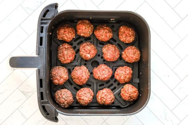 Frozen meatballs inside an air fryer basket.