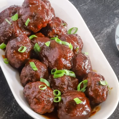 Meatballs smothered in rich tomato sauce garnished with chopped green onions.