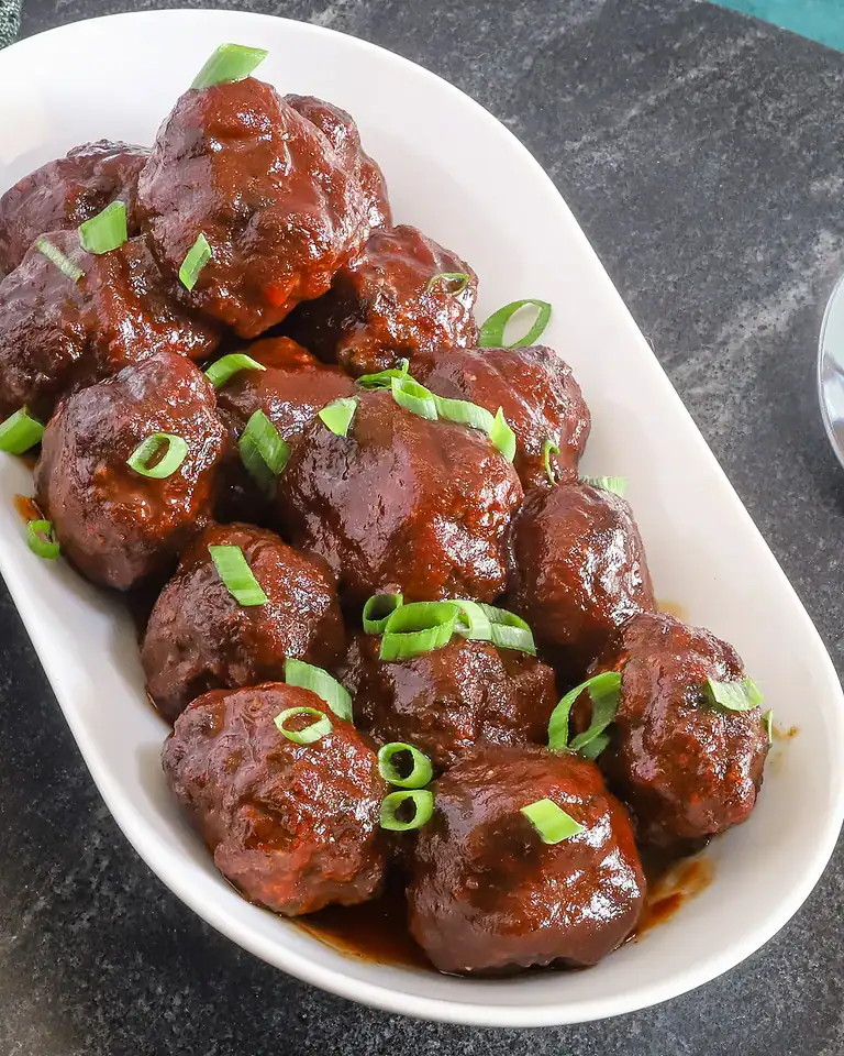 Meatballs smothered in rich tomato sauce garnished with chopped green onions.
