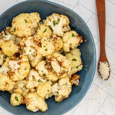 Roasted cauliflower florets in a blue bowl with herbs.