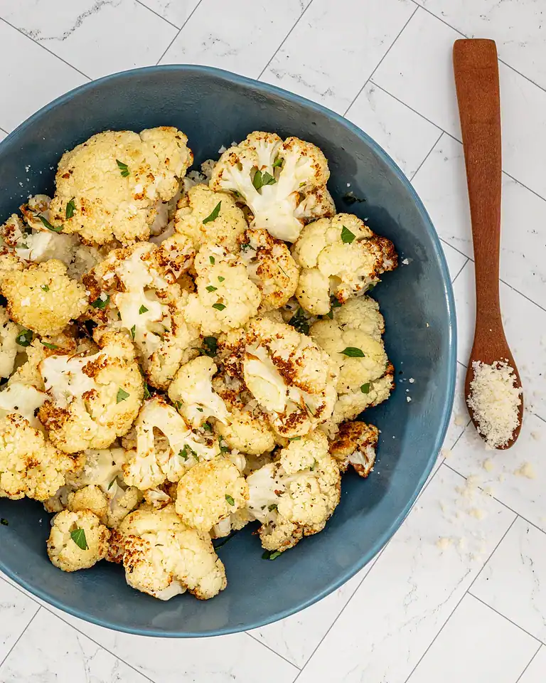 Roasted cauliflower florets in a blue bowl with herbs.