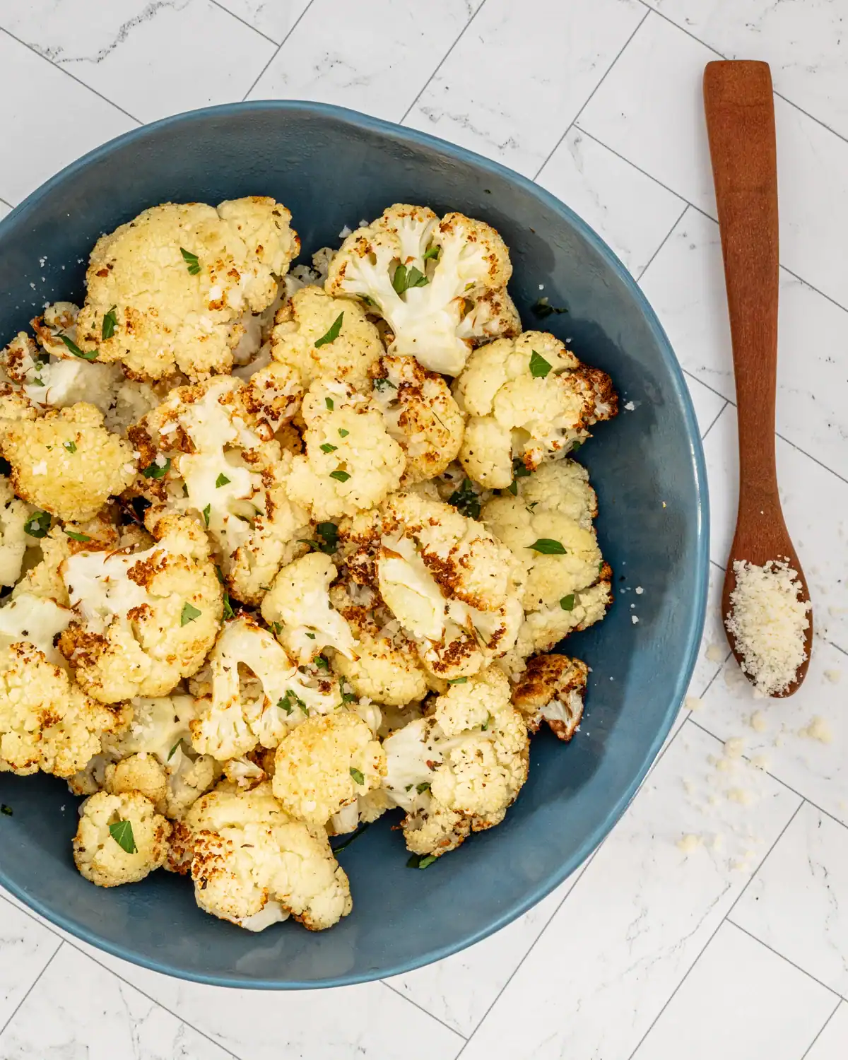 Roasted cauliflower florets in a blue bowl with herbs.