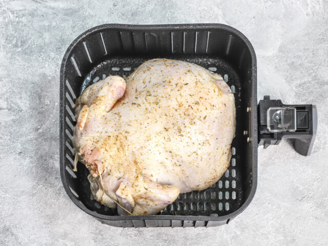 A whole chicken, seasoned, in the air fryer basket.